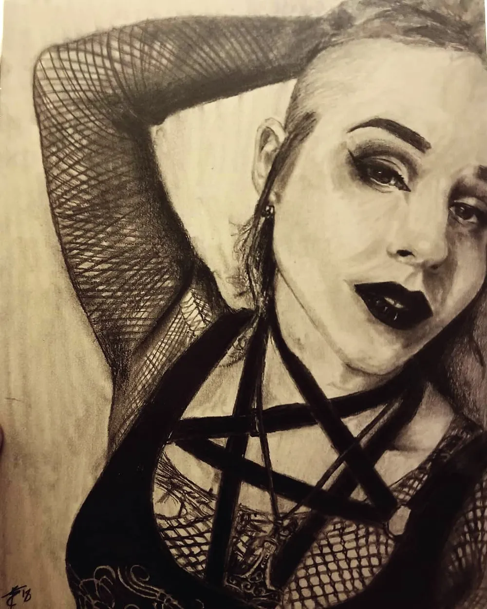 a woman with dark lipstick, one arm raised, wearing a fishnet sleeve and a strapped harness top